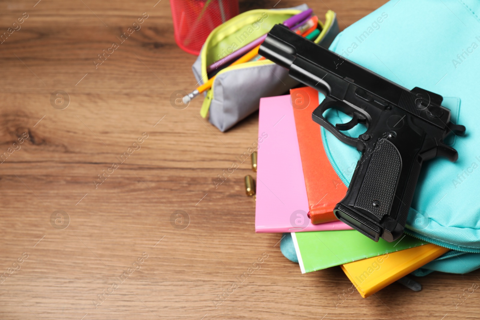 Photo of Gun, bullets and school stationery on wooden table, above view. Space for text