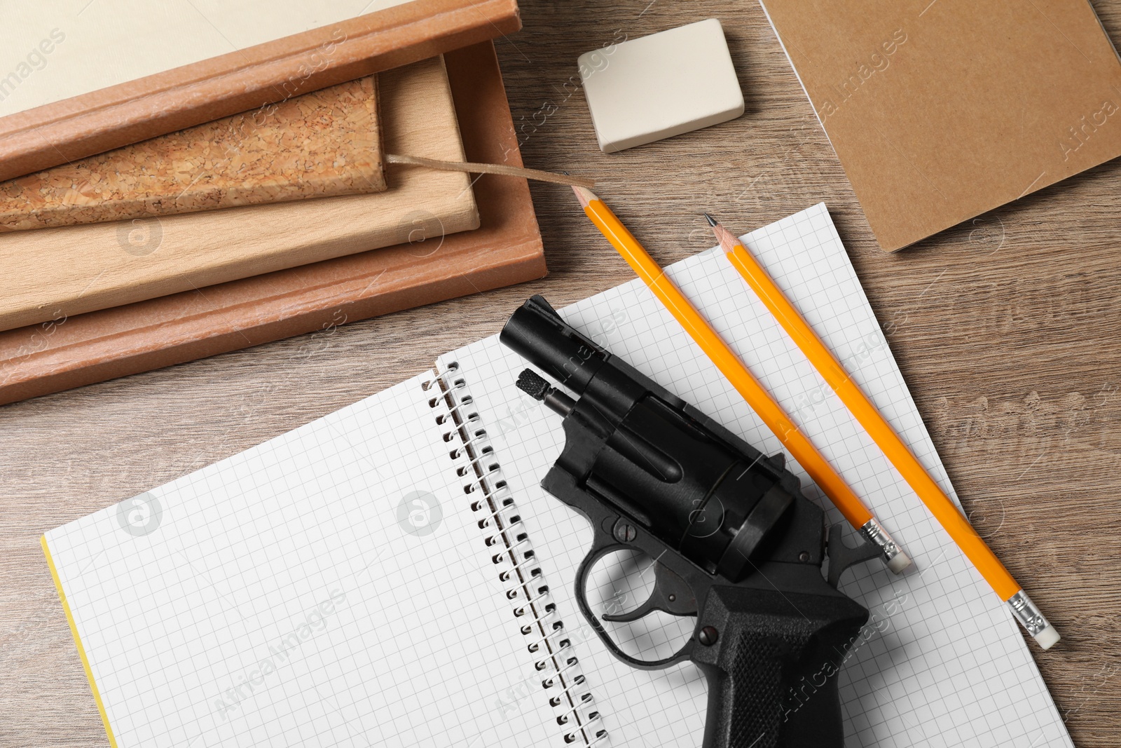 Photo of Gun and school stationery on wooden table, flat lay