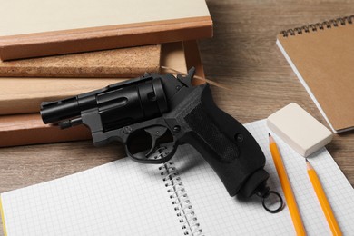 Photo of Gun and school stationery on wooden table, closeup