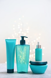 Photo of Set of hair care cosmetic products on gray table against light background with blurred lights, space for text