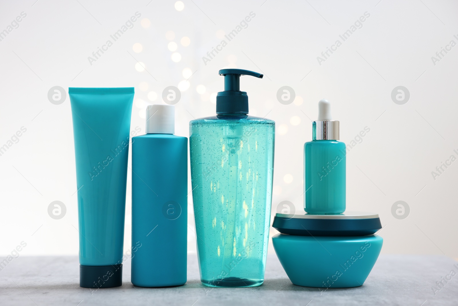 Photo of Set of hair care cosmetic products on gray table against light background with blurred lights