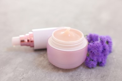 Photo of Set of different cosmetic products and ageratum flowers on gray table, closeup