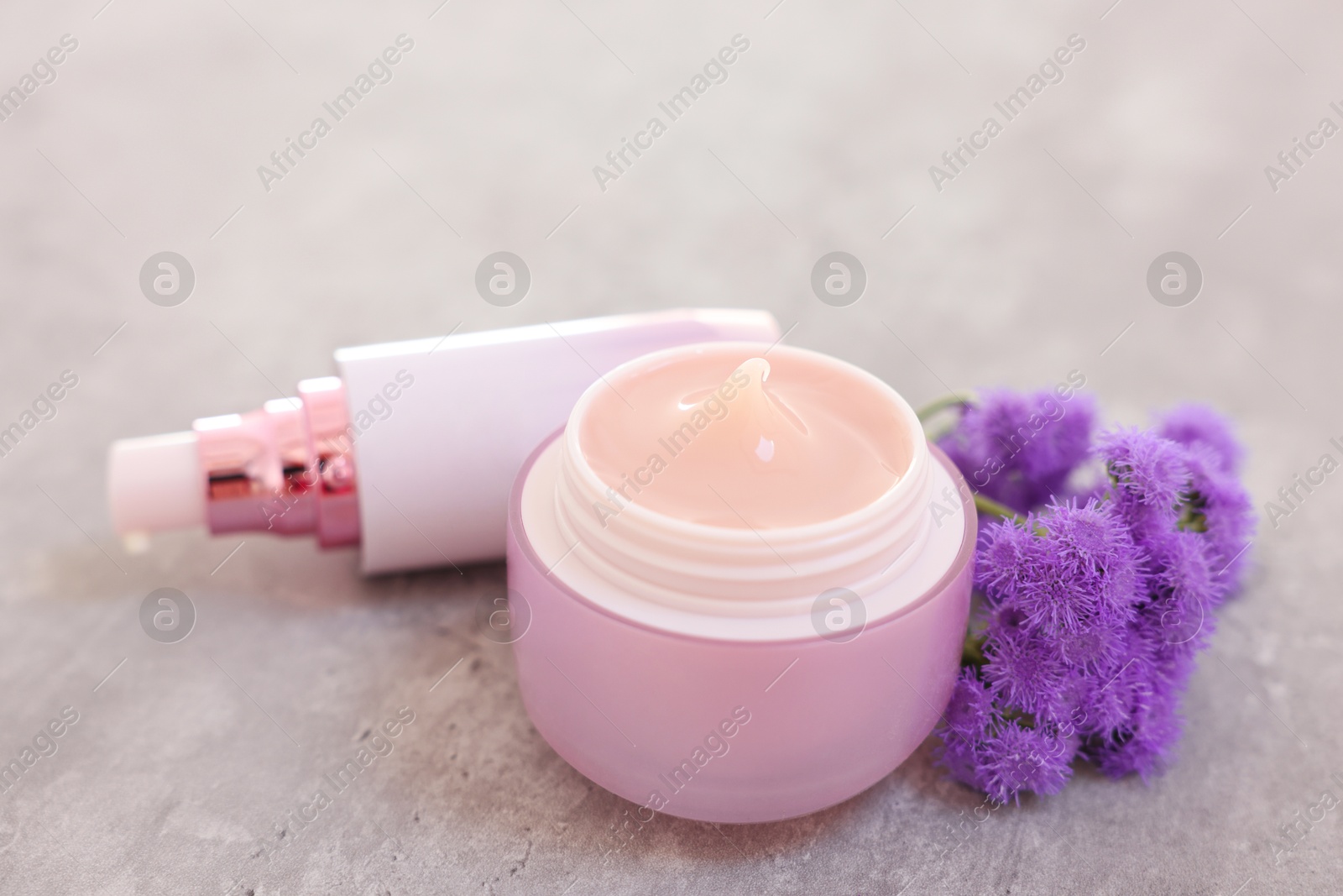 Photo of Set of different cosmetic products and ageratum flowers on gray table, closeup