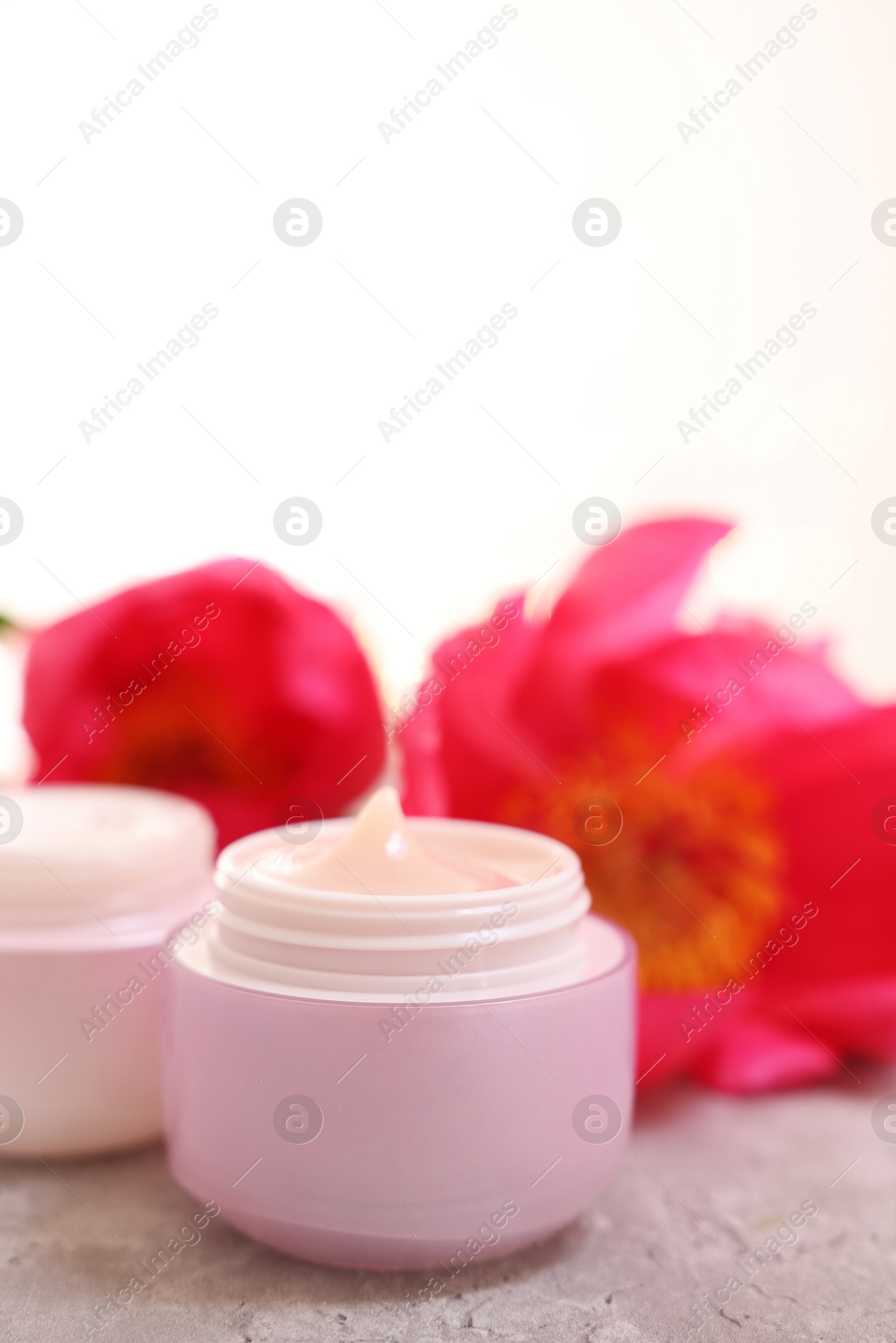 Photo of Jars of creams and peony flower on gray table against light background, closeup. Space for text