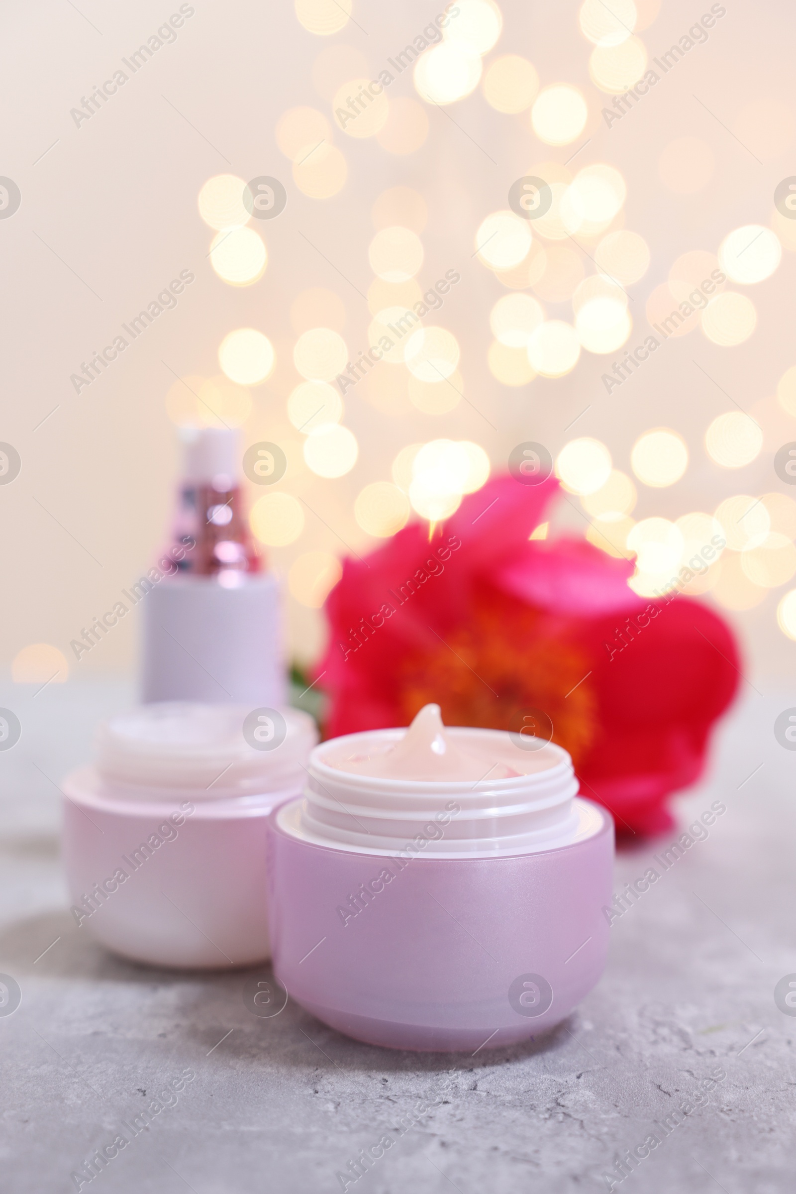 Photo of Set of different cosmetic products and peony flower on gray table against light background with blurred lights