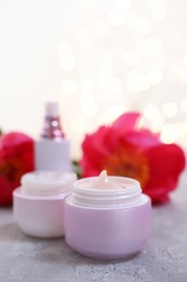 Set of different cosmetic products and peony flower on gray table against light background with blurred lights, closeup