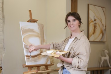 Portrait of smiling woman with palette near easel in drawing studio