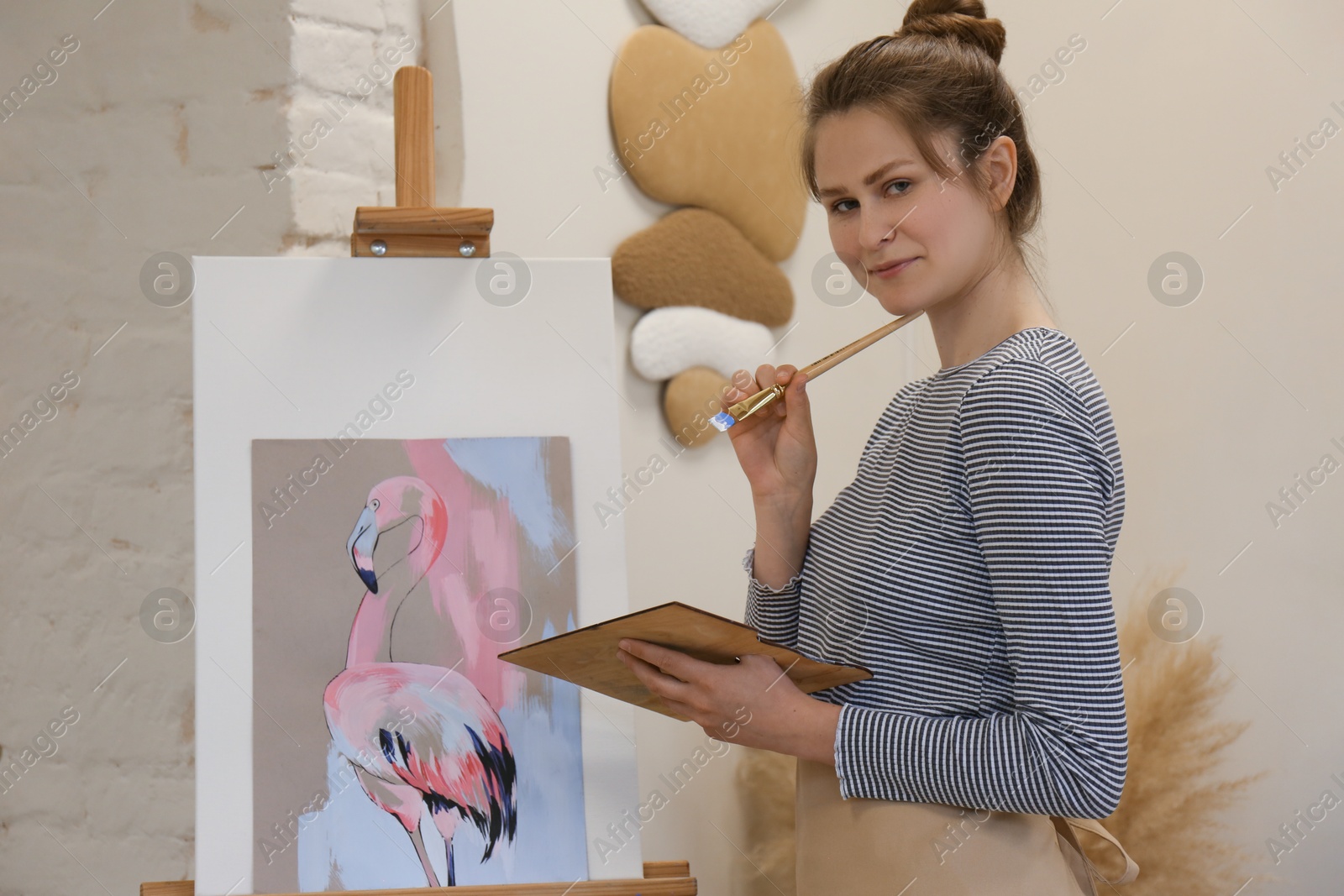 Photo of Portrait of woman with brush and palette near her artwork in drawing studio