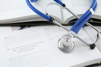 Photo of One medical stethoscope and books on table, closeup