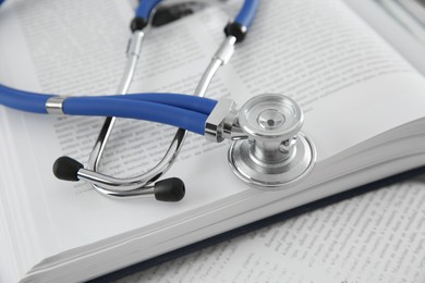 Photo of One medical stethoscope and books on table, closeup
