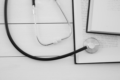 Photo of One new medical stethoscope and books on white wooden table, top view