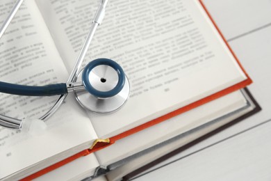 Photo of One new medical stethoscope and books on white wooden table, closeup