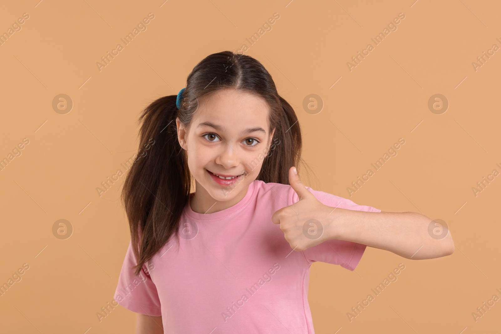 Photo of Portrait of beautiful girl showing thumbs up on beige background