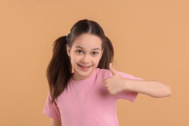 Portrait of beautiful girl showing thumbs up on beige background