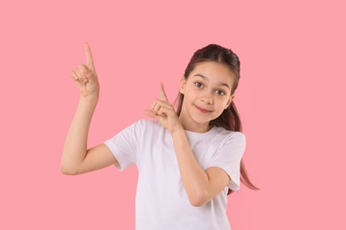 Portrait of beautiful girl pointing at something on pink background