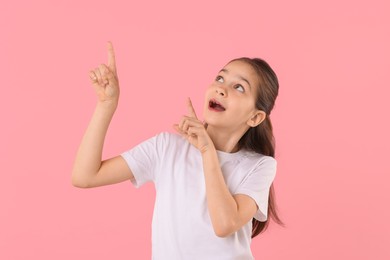 Emotional girl pointing at something on pink background