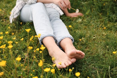 Photo of Woman sitting barefoot on green grass outdoors, closeup