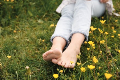 Woman sitting barefoot on green grass outdoors, closeup