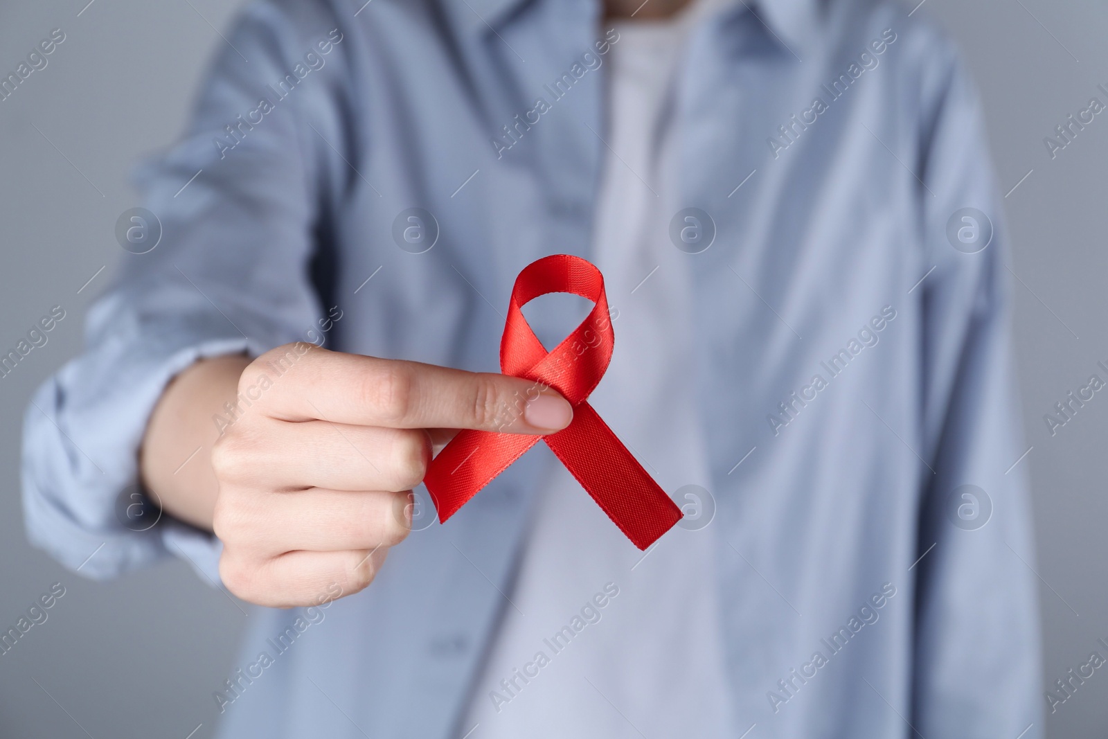 Photo of Woman with red awareness ribbon on grey background, closeup