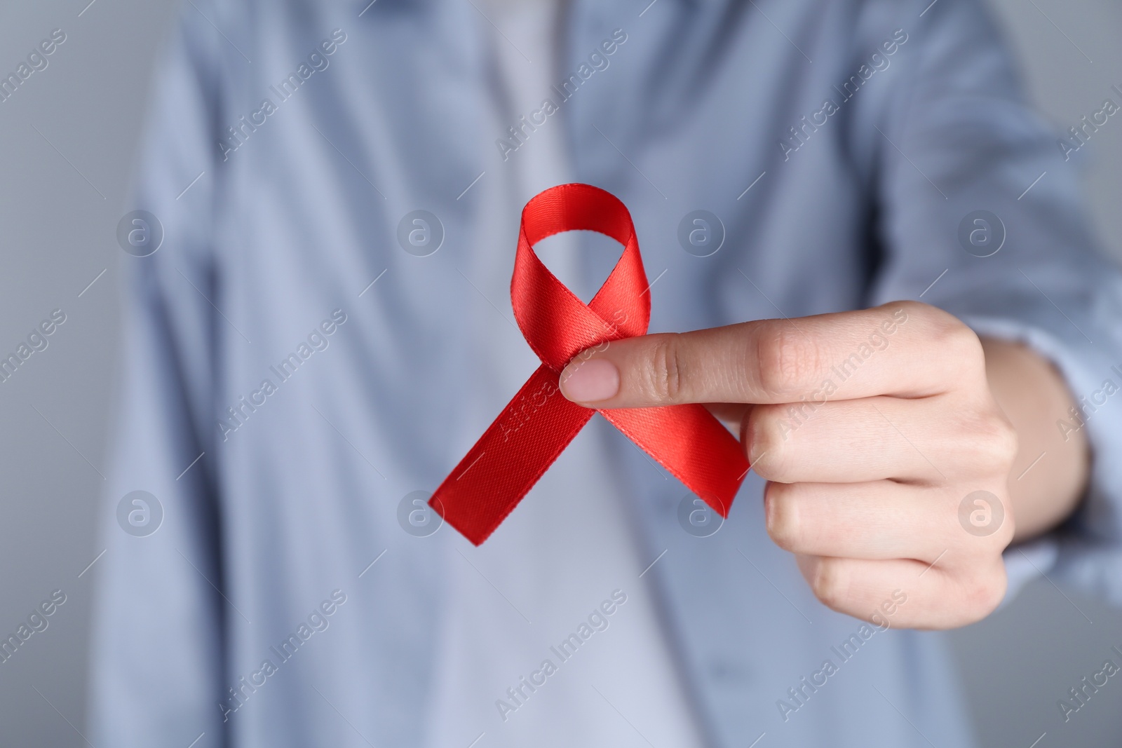 Photo of Woman with red awareness ribbon on grey background, closeup