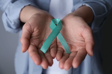 Woman holding turquoise awareness ribbon on grey background, closeup