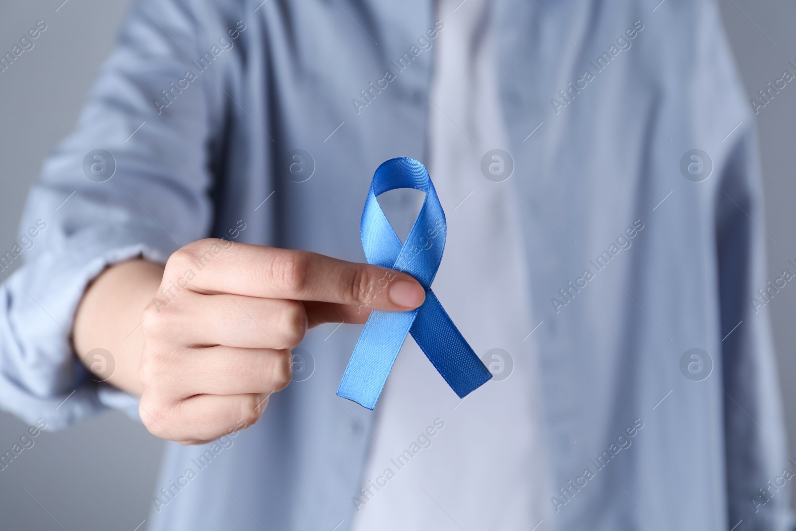 Photo of Woman with blue awareness ribbon on grey background, closeup