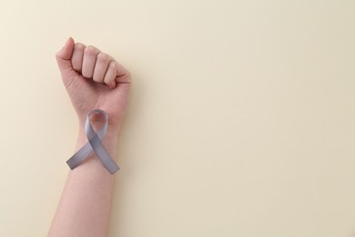 Woman with grey awareness ribbon on beige background, top view. Space for text