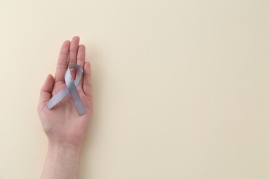 Woman with grey awareness ribbon on beige background, top view. Space for text