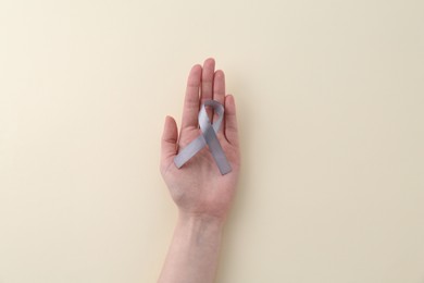 Photo of Woman with grey awareness ribbon on beige background, top view