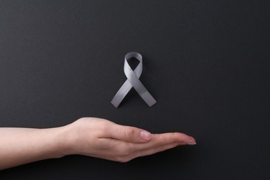 Woman with grey awareness ribbon on black background, top view