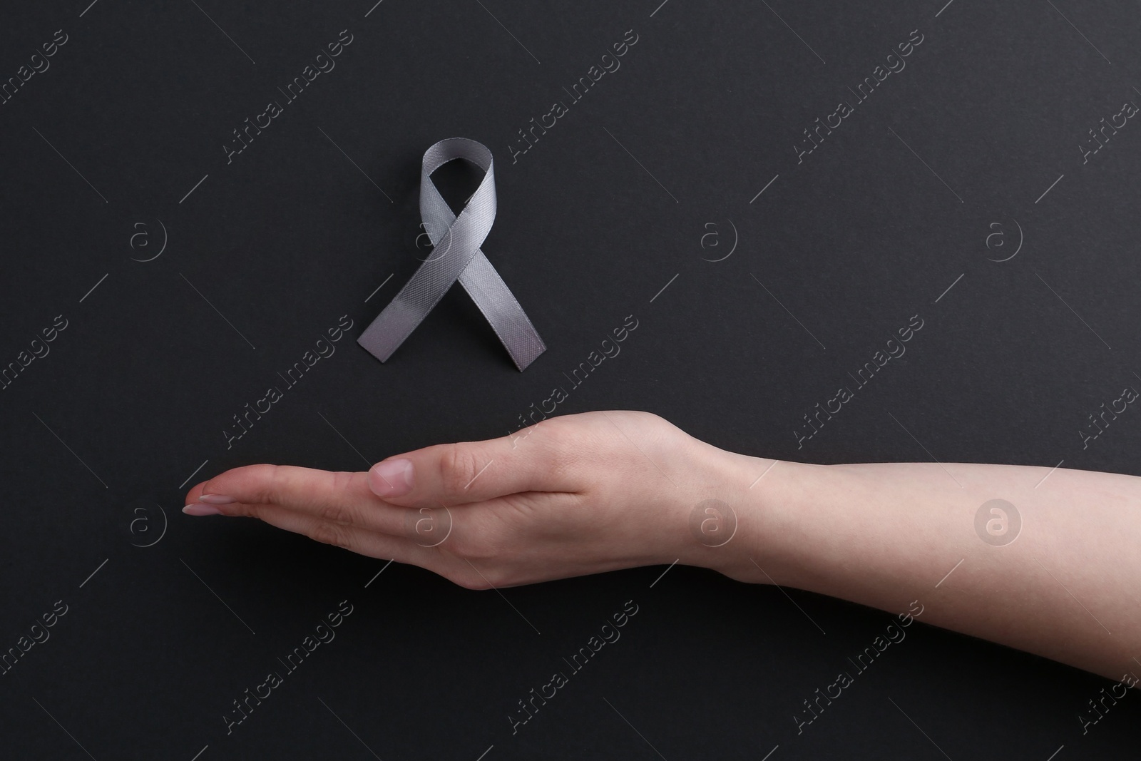 Photo of Woman with grey awareness ribbon on black background, top view