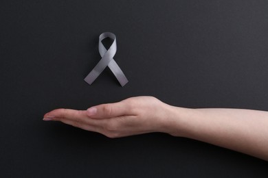 Woman with grey awareness ribbon on black background, top view