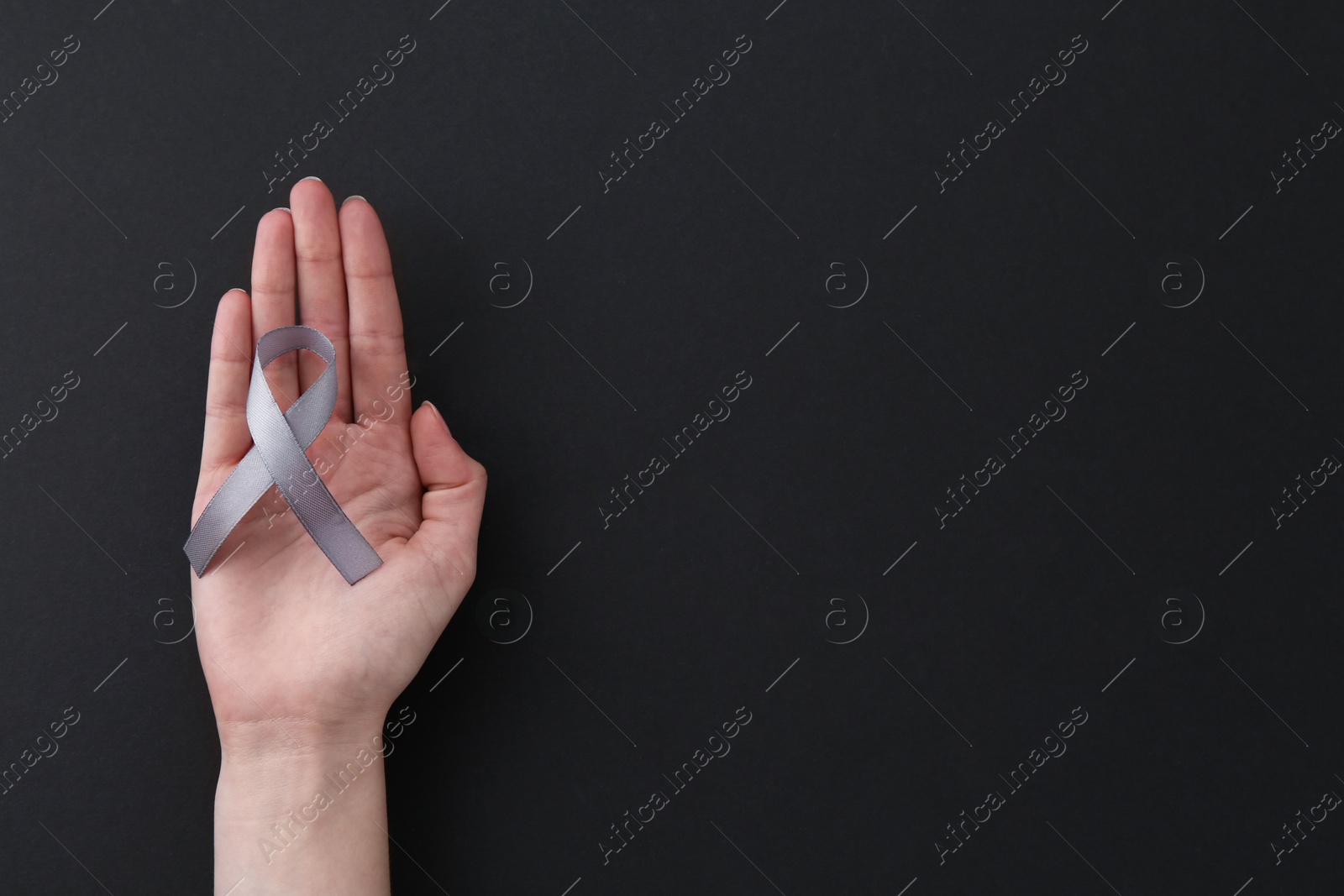 Photo of Woman with grey awareness ribbon on black background, top view. Space for text