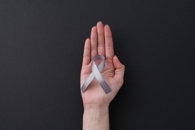 Photo of Woman with grey awareness ribbon on black background, top view