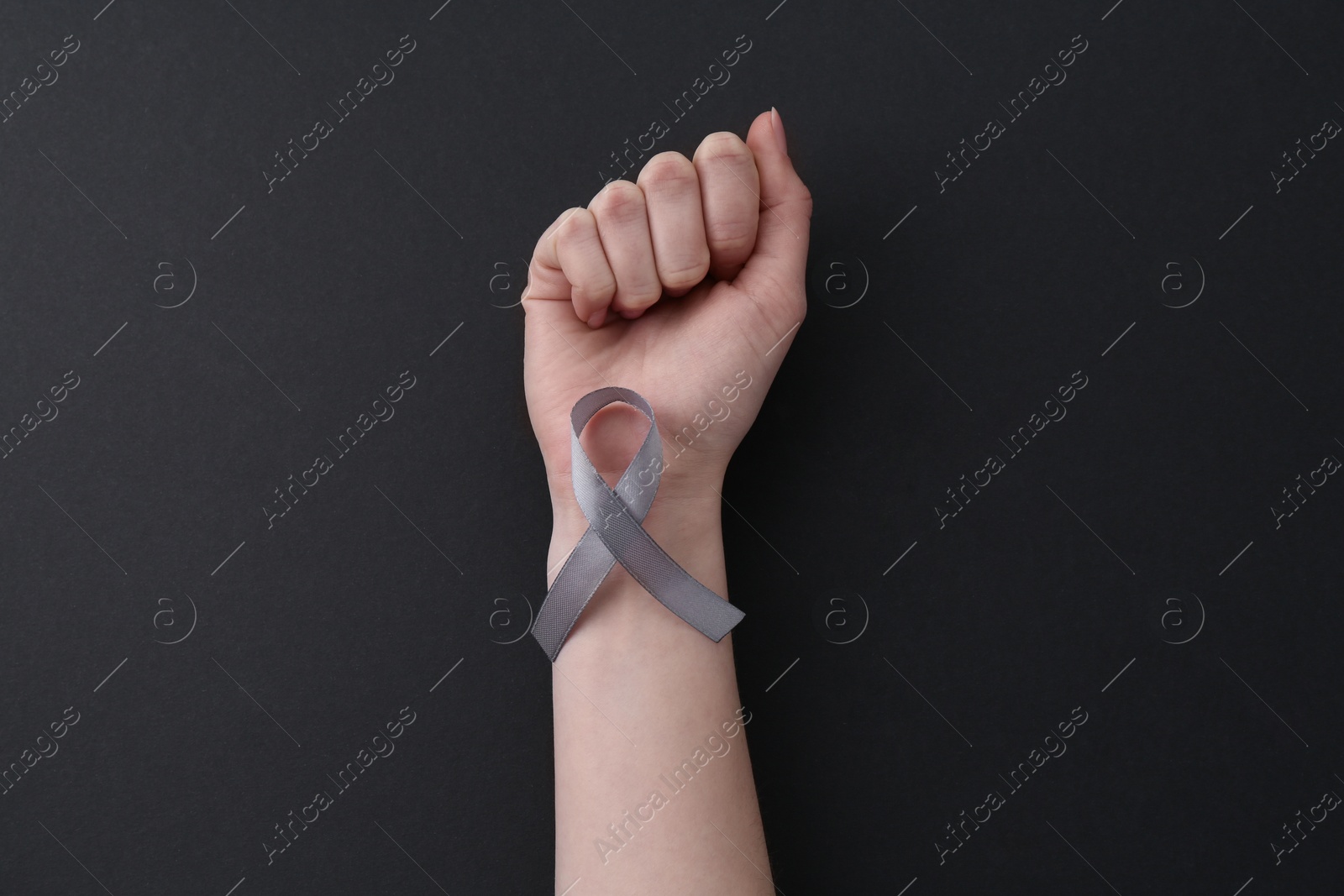 Photo of Woman with grey awareness ribbon on black background, top view