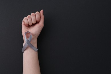 Photo of Woman with grey awareness ribbon on black background, top view. Space for text