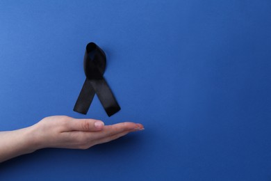 Woman with black awareness ribbon on blue background, top view. Space for text