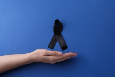 Photo of Woman with black awareness ribbon on blue background, top view. Space for text