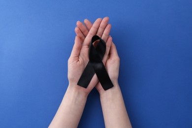 Woman with black awareness ribbon on blue background, top view