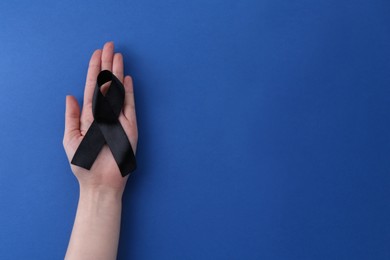 Photo of Woman with black awareness ribbon on blue background, top view. Space for text