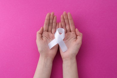 Photo of Woman with white awareness ribbon on pink background, top view