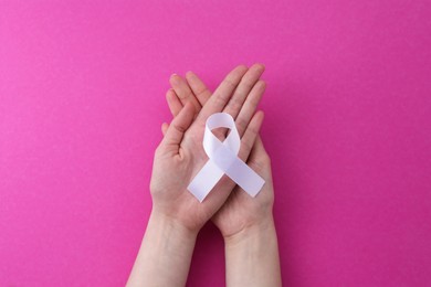 Woman with white awareness ribbon on pink background, top view