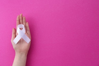 Photo of Woman with white awareness ribbon on pink background, top view. Space for text