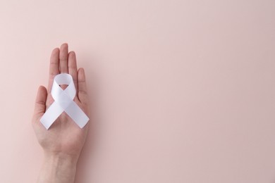 Photo of Woman with white awareness ribbon on beige background, top view. Space for text