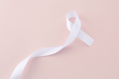 Photo of One white awareness ribbon on beige background, above view