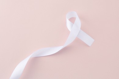 One white awareness ribbon on beige background, above view