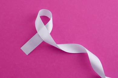 Photo of White awareness ribbon on pink background, top view