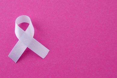 Photo of White awareness ribbon on pink background, top view. Space for text