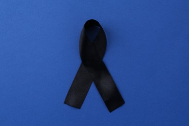 Photo of Black awareness ribbon on blue background, top view