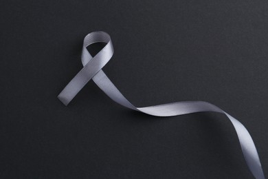 Photo of Grey awareness ribbon on black background, top view